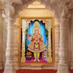 Bhagwan Swaminarayan standing in colourful traditional attire inside an ornate golden temple arch with floral offerings.