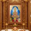 Swaminarayan Maharaj in white and gold devotional attire inside a blue temple alcove with golden ornamentation and flower offerings.